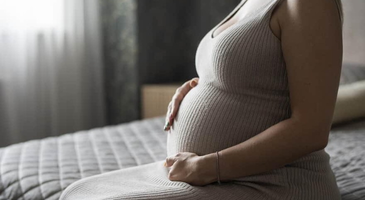 Empregada gestante assegurada sentada na cama de seu quarto